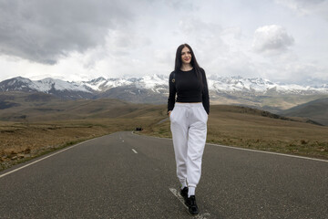 Woman standing on the road, beautiful snow-capped mountains in the background. Vacation in the mountains.