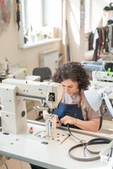 A woman tanner sews a leather belt on a sewing machine. Vertical photo.