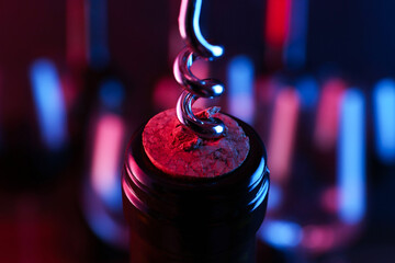 Wine bottle with corkscrew in lights on blurred background, closeup