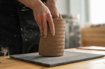 Close-up of a man's hands making a patterned cylinder out of clay. 