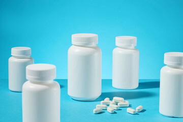 A set of white unlabeled medicine jars scattered placing on the table, a cluster of white tablets in center, against on blue background. The photo for medicine products branding, front view