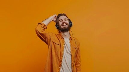 A joyful man in a mustard yellow shirt enjoys his music with enthusiasm, headphones on, against a bright orange background.