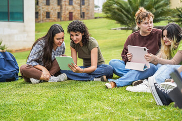 Naklejka premium Caucasian students studying with digital tablets sitting on grass at college campus park - Back to school concept - Main focus on right girls faces