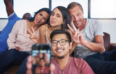 Business people, happy and selfie in office with peace, diversity and sofa for playful, joy and fun. Creative agency, smile and team in workplace with memory for collaboration, cooperation or startup