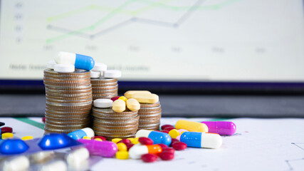 Colorful pills and capsules on a pile of coins and scattered around stack of coins for health...
