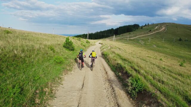 Two cyclists men riding electric bikes outdoors. Back view of male tourists biking in the mountains, wearing helmets and backpacks. Concept of sport, active leisure and nature.