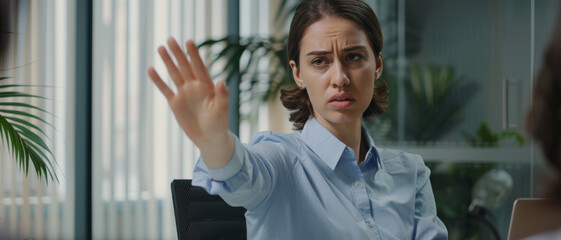 A businesswoman raises her hand, signaling to stop during a serious conversation, with a focused expression in an office setting.