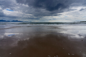 Waves roll up Llanddwyn beach, Anglesey, under dark threatening clouds.