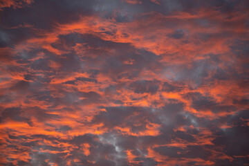 fiery sunset lights on layered clouds with hints of blue sky showing behind