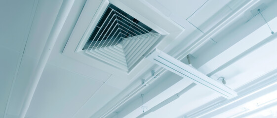 Obraz premium Geometric air conditioning vent on a modern ceiling, accentuated against a clean, white background with sleek, linear architecture.