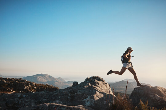 Hiking, woman and jump on rocks for fitness, wellness and energy at sky mockup. Trekking, female athlete and confident on mountain with gap, travel or adventure in nature space for exercise or growth
