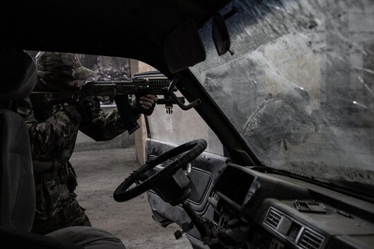 Two military men in camouflage take aim at an enemy near a crashed car. Soldiers over the vehicle. Special forces at special operation.