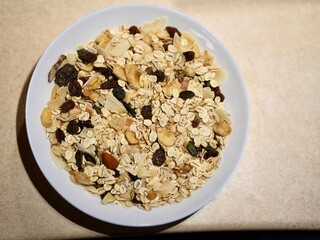 Dry oatmeal with nuts and dry fruit on white plate on table.