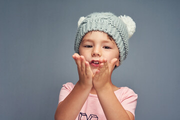 Happy boy, portrait and blowing kiss with fashion, style or clothing on gray studio background. Little child, kid or youth with love, beanie or winter cap in care, gratitude or childhood on space