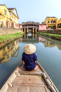 Old man with conical hat on a boat looking at famous japanese bridge in Hoi An, Vietnam