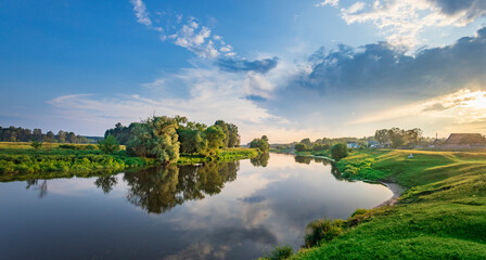 A tranquil river winds through a lush, green landscape, reflecting the blue sky and fluffy clouds...