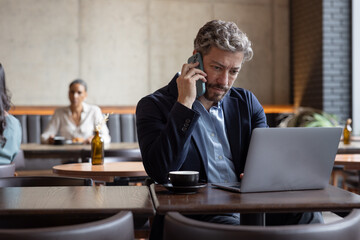 Mature hispanic male businessman working from a cafe making a phone call