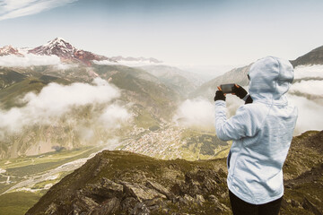 Close-up natural portrait of one young female tourist in cold autumn mountains, takes smartphone...