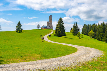 A winding gravel path leads up to the Dalimil Lookout Tower in Czechia, surrounded by lush green...