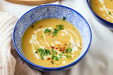 Two bowls of creamy potato soup, spoons, napkin and wooden cutting board with a loaf of bread and cut pieces. The surface of the soup is decorated with cream, croutons, parsley and ground red pepper.