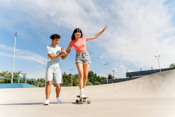 Fototapeta premium Happy teenage couple riding short modern skateboards at the skate park