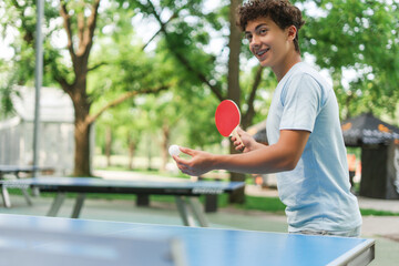 Happy teenager boy playing ping pong holding ball and racket in his hands