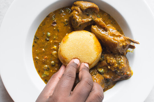 Overhead view of nigerian ogbono soup and eba on a white plate, top view of ogbono draw soup with garri and assorted meats in a soup plate, flatlay of nigerian ogbono and okra soup