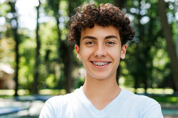 Positive teenager boy with braces looking at camera in the park
