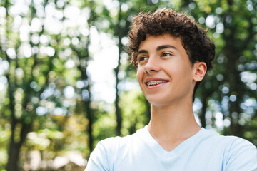 Smiling teenager boy with braces looking to the side outdoor, copy space