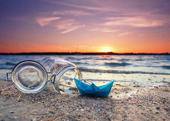 blue paper boat with a glass at the sandy beach in sunset
