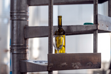 A Yellow Bottle and Glass Resting on Metal Shelf in Industrial Winery Setting