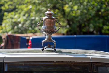 Naklejka premium Antique Silver Trophy Positioned on Car Roof in a Lively Outdoor Setting During Daylight