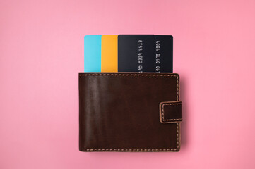 Brown leather wallet with colored plastic debit and credit bank cards on pink background, top view flat lay. Minimalistic concept of shopping, online payment. Stylish unisex wallet