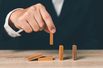 Risk and strategy in business, Close up of businessman hand removing wooden block domino..Domino of...