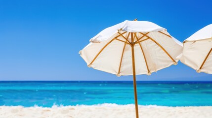 Four white beach umbrellas on a pristine sandy beach with turquoise water and a clear blue sky. Idyllic tropical vacation concept.