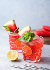 Two glasses watermelon cocktail with lime, ice and mint on a blue  background with fruits.