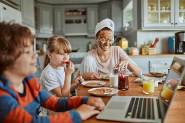 Mom with face mask and kids having breakfast while watching laptop