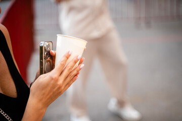 A woman expertly balances a steaming cup of coffee in one hand while using a smartphone in the other, demonstrating her impressive multitasking skills in a techdriven setting