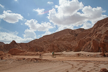 Naklejka premium cyclers biking at the desert in front of rocky mountain at Atacama desert in Chile 