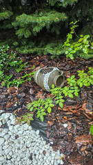 Fototapeta premium Decorative jug in the garden near flowers and trees. Rainy weather.