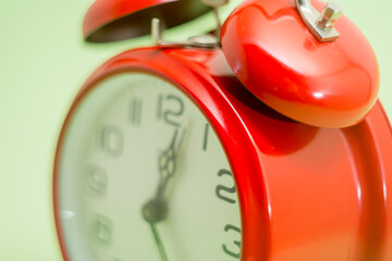 A close-up of a red, vintage alarm clock with black hands and numbers, slightly tilted to the...