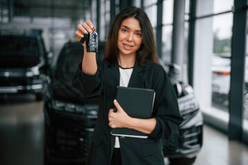 Front view, holding keys. Saleswoman in car showroom, selling automobile
