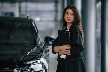 Notepad in hands. Saleswoman in car showroom, selling automobile