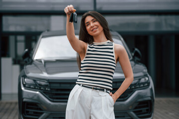 Happy owner of the new car with keys. Attractive young woman is outdoors near her brand new car