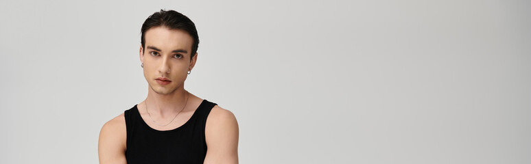 A man with short dark hair poses in a black tank top against a white background.