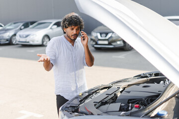 Frustrated driver calling for help with broken down car in parking lot