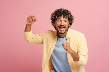 Excited young Indian adult man celebrating success with fists raised on pink background