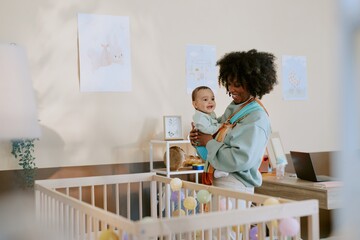 Young African American mother playing with her child while carrying him in multicolored sling