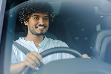Attractive, smiling Indian man driving car in city, transportation concept