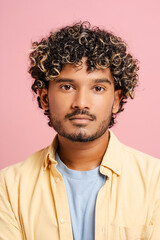 Fototapeta premium Portrait of Indian adult male with curly hair posing on pink background